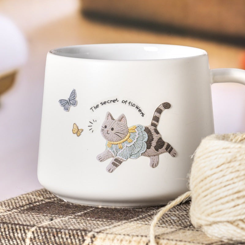 StationeryHaul cat sticker featuring an embroidered-style kitten with butterflies on a white ceramic mug