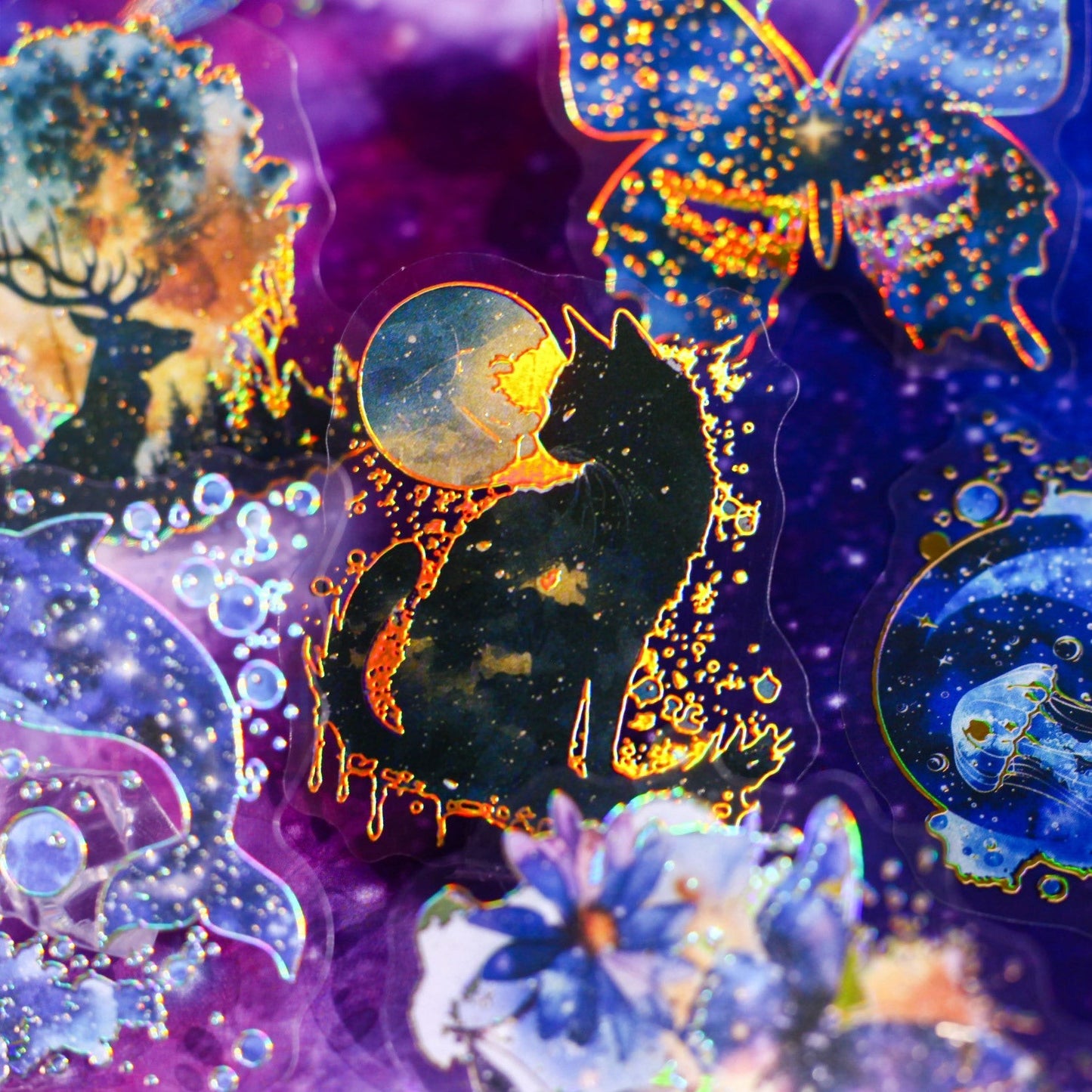 StationeryHaul holographic transparent stickers featuring a black cat, dolphin, jellyfish, butterfly, and deer in celestial galaxy designs with purple, blue, and gold.