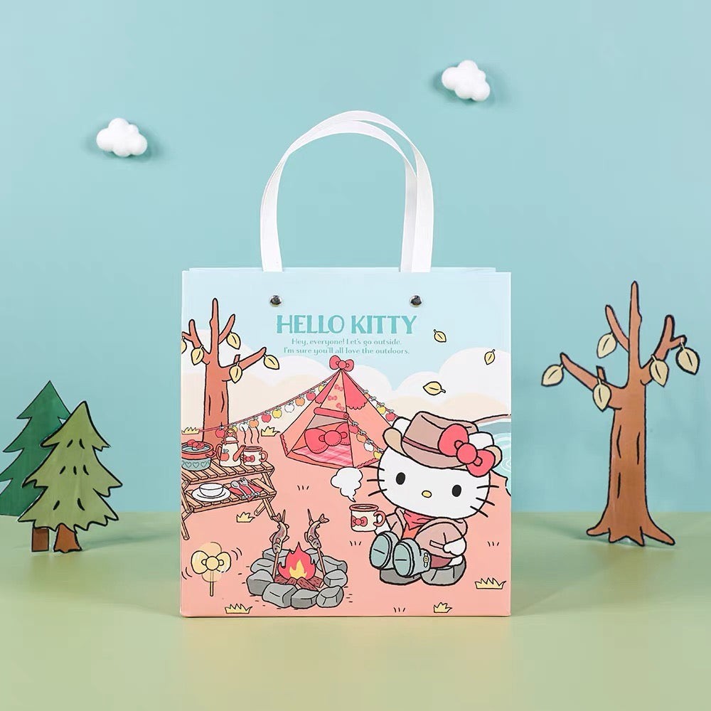 StationeryHaul light blue paper gift bag with Hello Kitty camping scene. Features Hello Kitty in a hat and scarf by a campfire and tent.